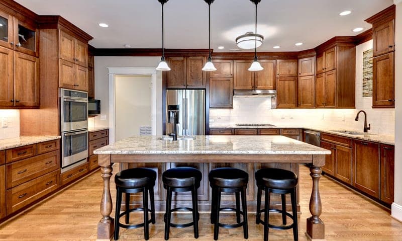 Kitchen with wood cabinetry, stainless appliances, and a granite island seating four